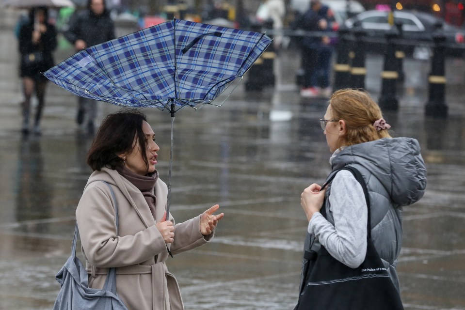 A woman battles with her umbrella in London's Trafalgar Square today as most parts saw a wet and windy day