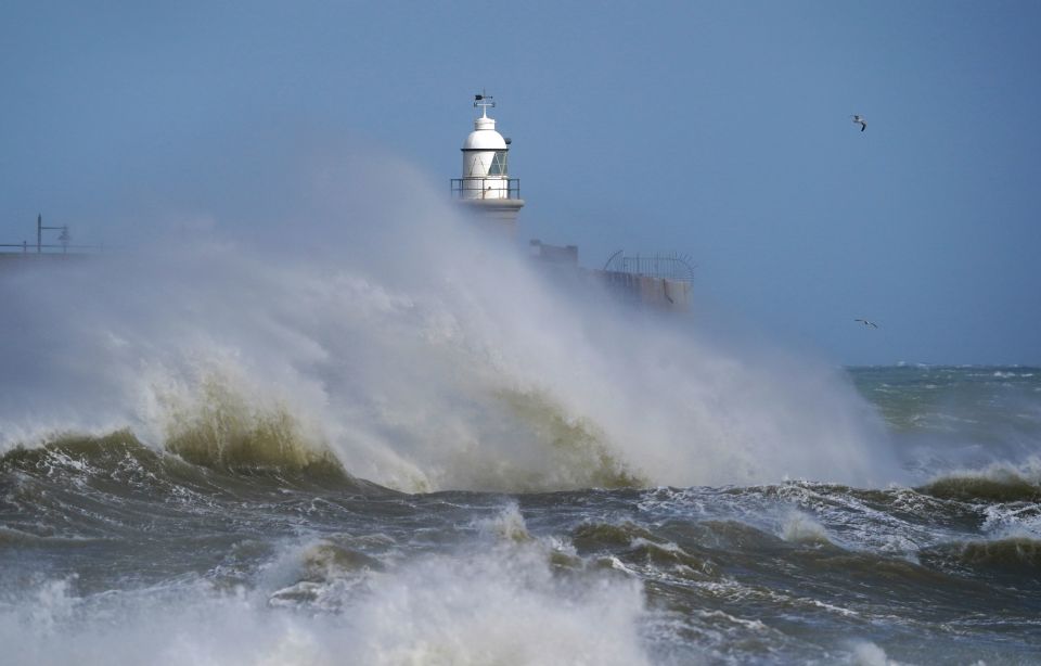 Waves crash around a lighthouse in Folkestone, Kent this morning