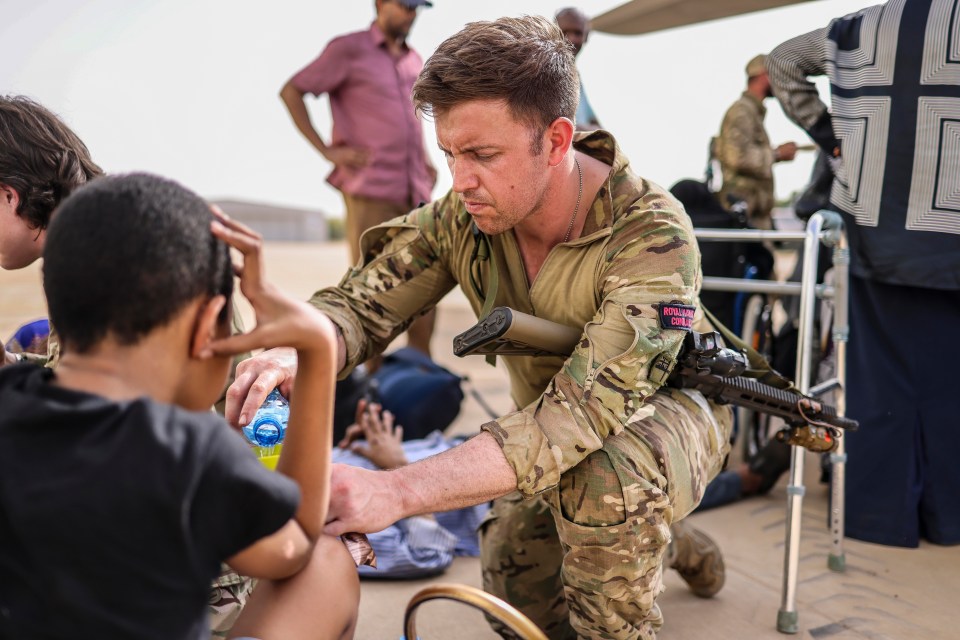 A commando dishes out water to children on the tarmac of the airport