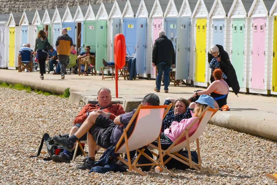 Pals relax in deckchairs on the beach at Lyme Regis, Dorset, today