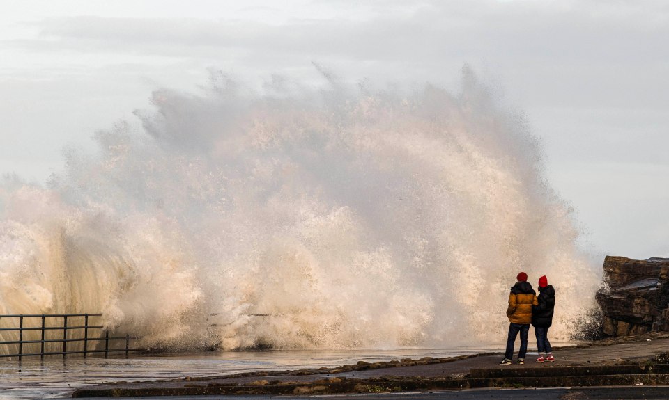 Locals look on as big waves crash into the promenade at Whitley Bay