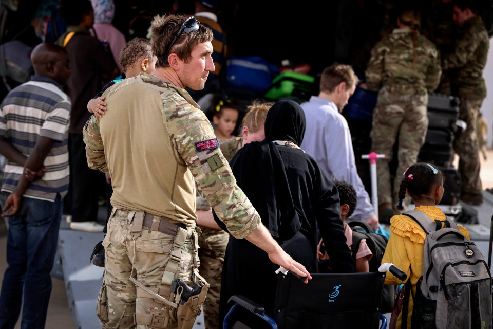 A Royal Marine cradles a child as he helps guide Brits onto the evacuation plane