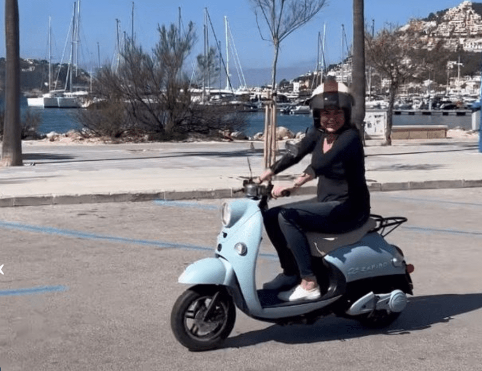 Amanda was riding the baby blue scooter while sporting a navy blue long sleeve blouse, some indigo blue pants, written plimsolls, and a cream helmet