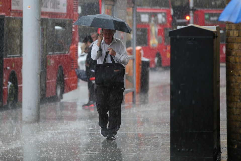 A man shelters under an umbrella as the rain comes down in central London