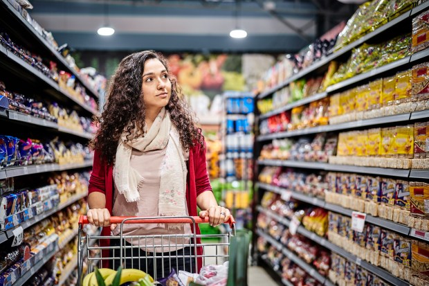 Woman with shopping cart in supermarket aisle. Female customer is looking at groceries in store. She is wearing casuals.