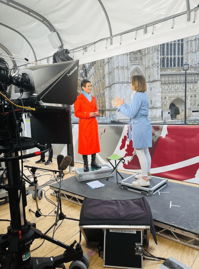 A behind-the-scenes snap shows Naga standing on a metal box to prop her up, making her taller on screens