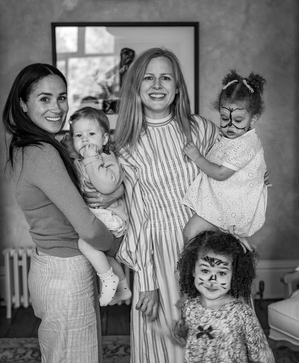 Meghan holds Lilibet while standing with Camilla Holmstroem, wife of the couple's preferred photographer, and her two daughters