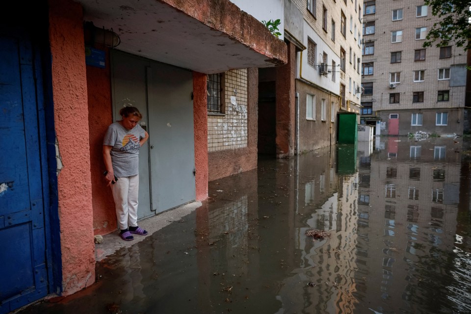 A woman seen standing next to the entrance to her house on a swamped street