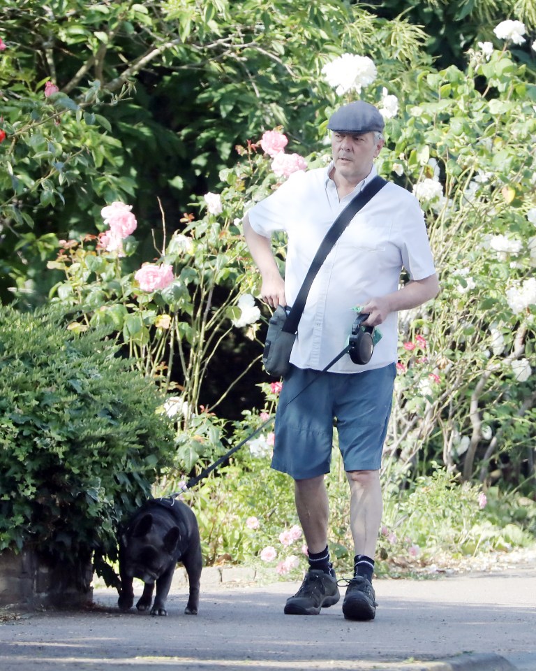 He kept the pet pooch on a lead as he strolled down a pretty street lined with flower bushes