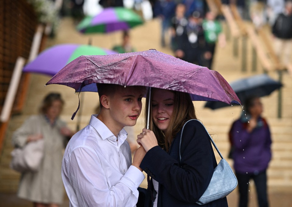 Visitors huddled under an umbrella as Wimbledon grounds are battered with rain today