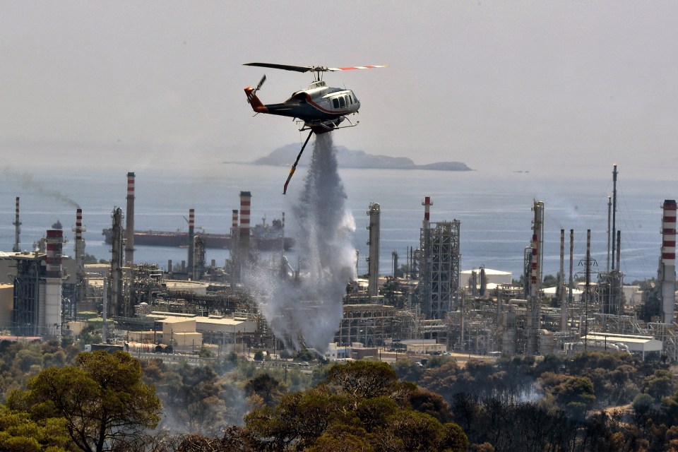 A firefighting helicopter sprays water during a forest wildfire near an oil refinery in Agioi Theodoroi