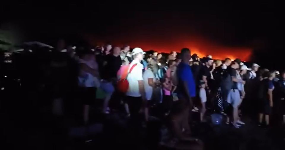 A menacing red glow lights up the sky behind the evacuees caused by flames nearing the beach