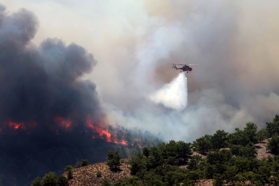 A helicopter dumps water on the raging inferno engulfing large areas of Rhodes