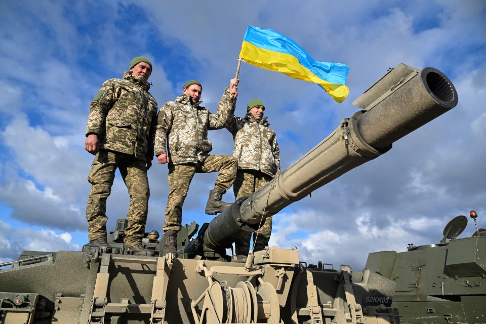 Ukrainian personnel hold a Ukrainian flag as they pose on top of a Challenger 2 tank during training at Bovington Camp, near Wool in southwestern Britain, February 22, 2023. REUTERS/Toby Melville