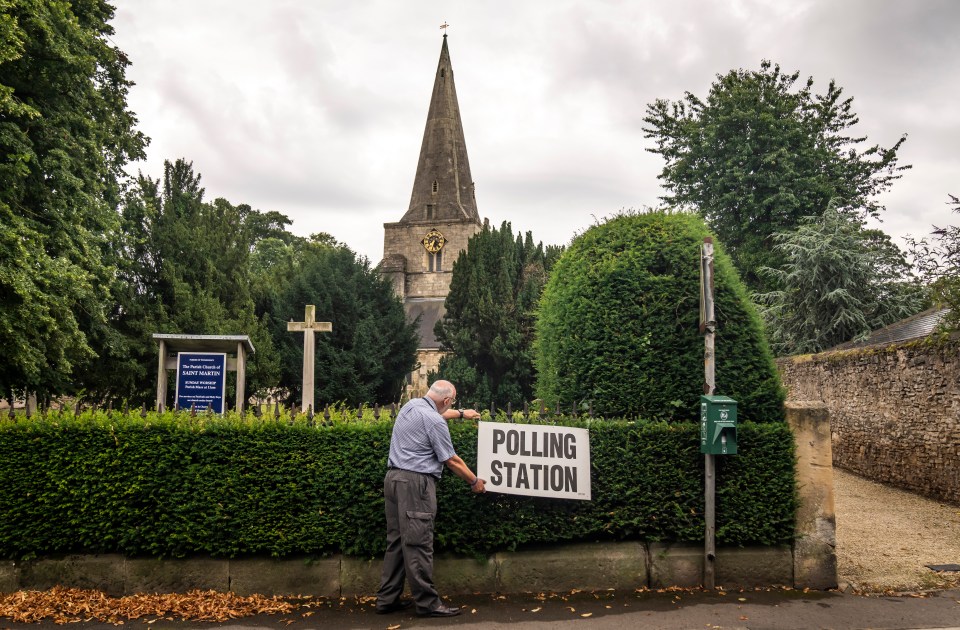 A local adjusts a polling station sign at Saint Martin Church in Womersley, part of the Selby and Ainsty constituency in North Yorkshire