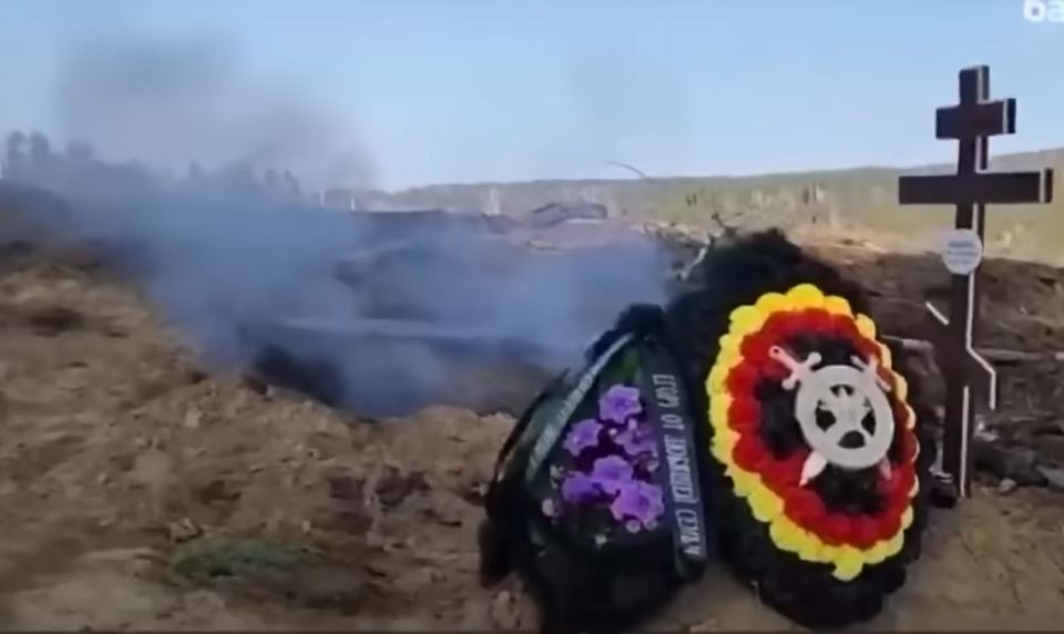 A Wagner wreath is seen at a grave site with an open ditch cooking behind it