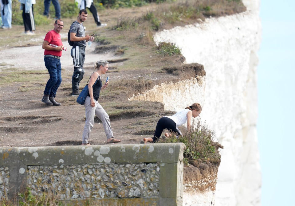 Daft teenagers hang over a 150ft sheer cliff edge as adults watch on grinning