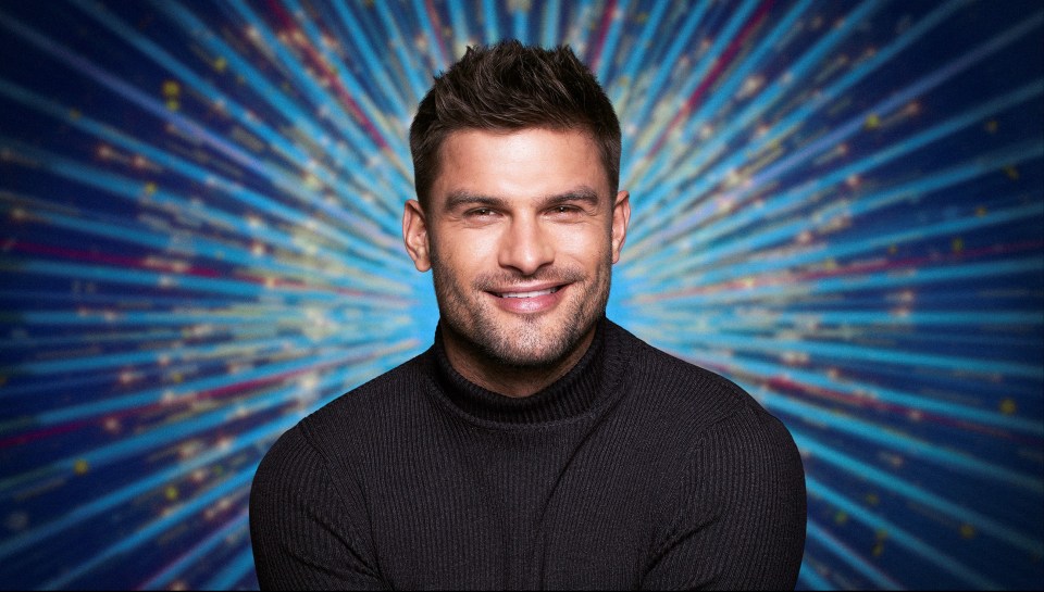 a man in a black turtleneck smiles in front of a blue background