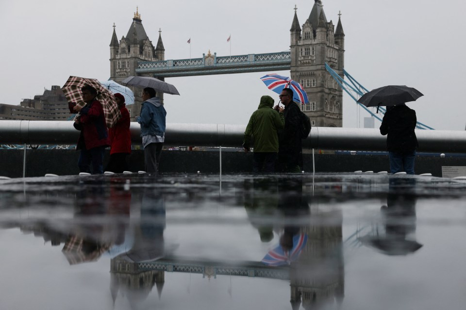 Soggy tourists take in a grey Tower Bridge in London on Monday - the capital will be thumped by thunderstorms and rain