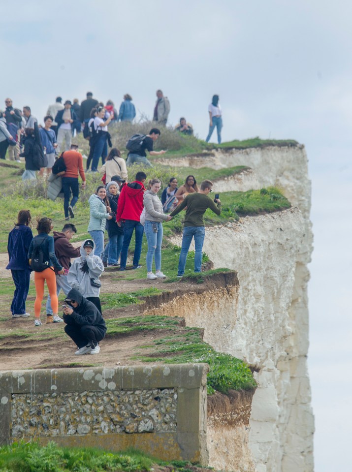 One woman holds onto a man as he leans over the cliffs to get a picture