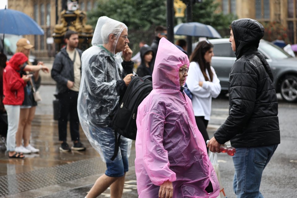 Tourists try and take cover from the rain at Westminster Bridge, London, on Sunday