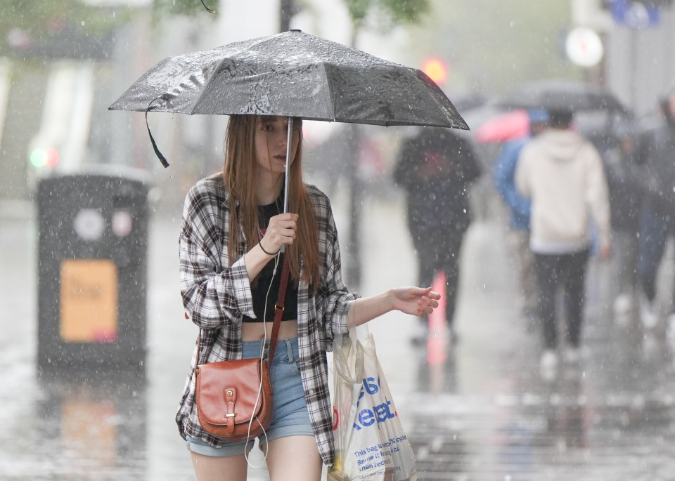 A woman sheltered herself from the rain during a downpour in Manchester today