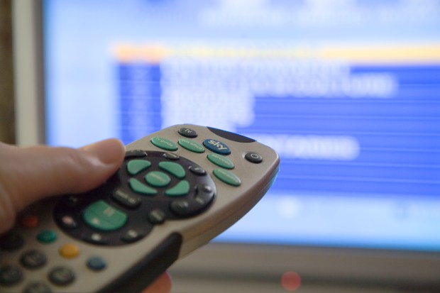 a person is holding a sky remote control in front of a television