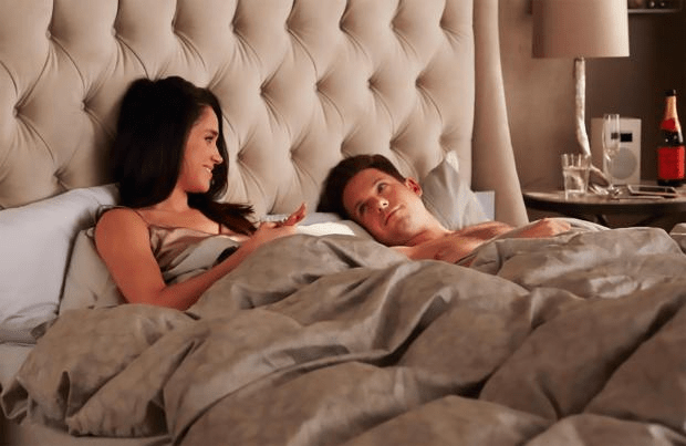 a man and a woman are laying in bed with a bottle of champagne on the nightstand