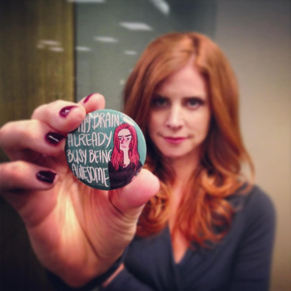 a woman holds up a button that says " my brain already busy being awesome "