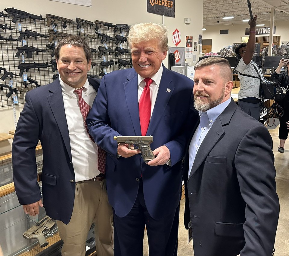 Donald Trump smiles as he holds a gun with his face etched onto the handle