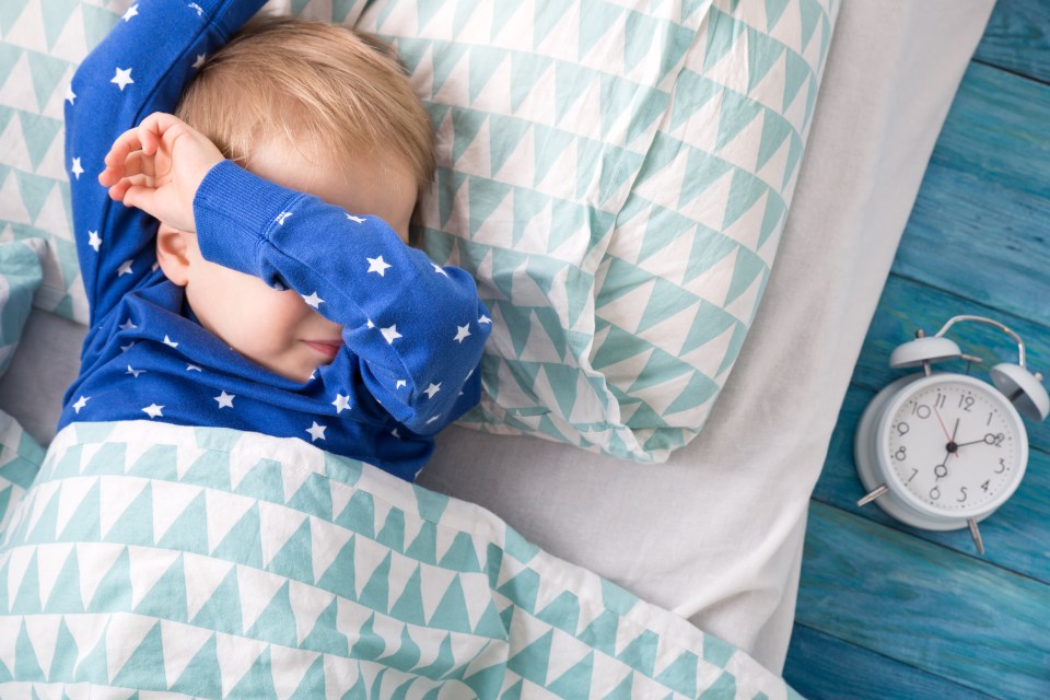 Three years old child crying in bed. Boy hiding and closing eyes with hands