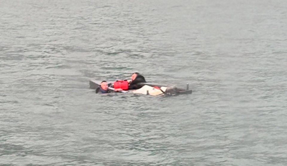 Dramatic pictures show the moment before two men were rescued at sea by a passing ferry after they were found gripping onto the sides of a sinking dinghy