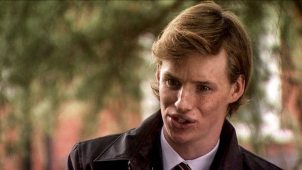 a young man in a suit and tie is standing in front of a tree .