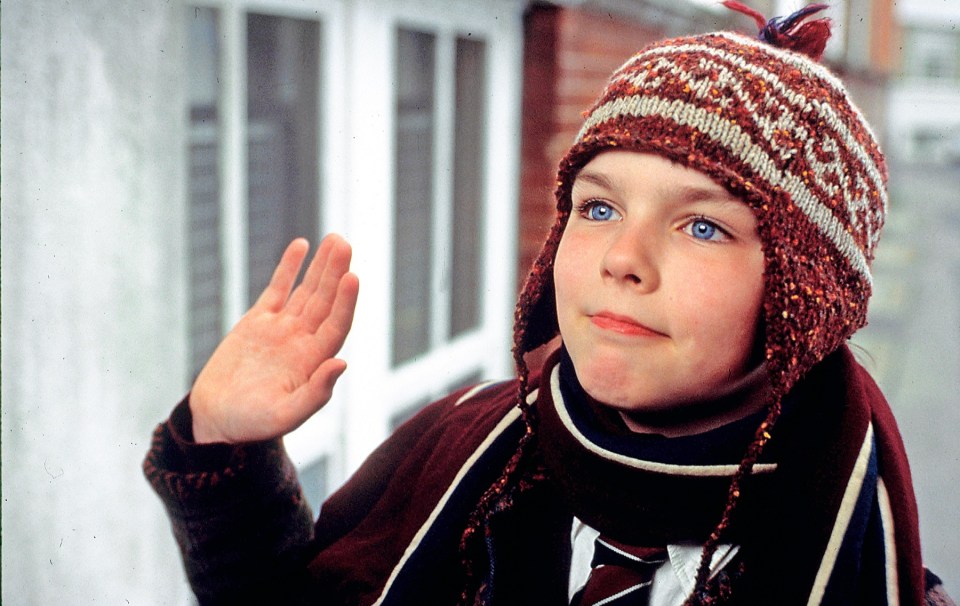 a young boy wearing a knitted hat and scarf waves his hand