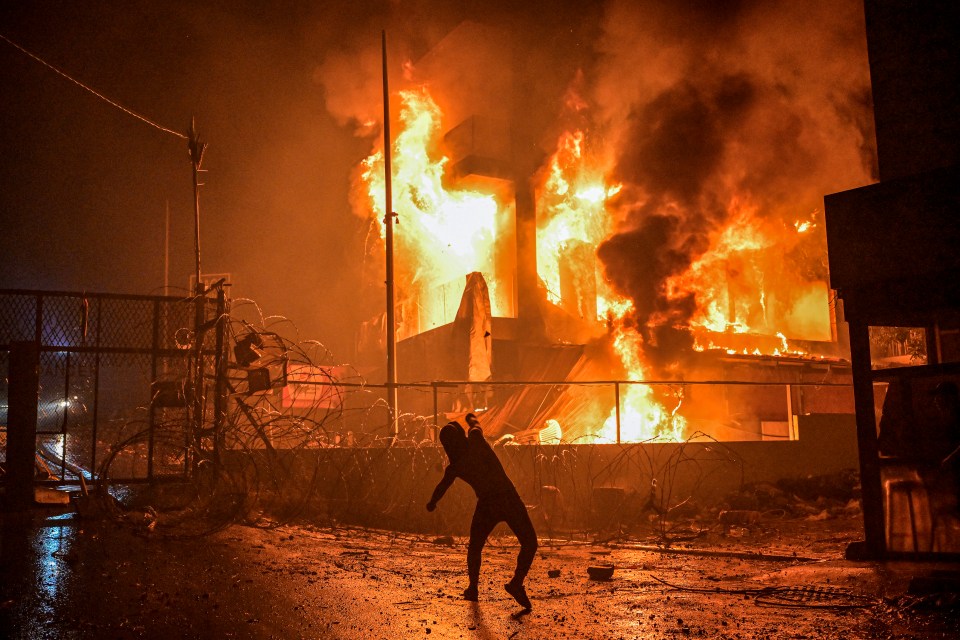 A protester hurls stones at a burning building just outside the US Embassy in Lebanon