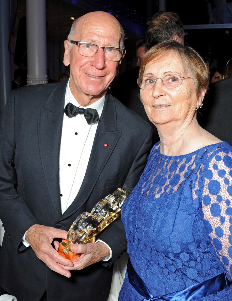 a man in a tuxedo holds a trophy next to a woman in a blue dress