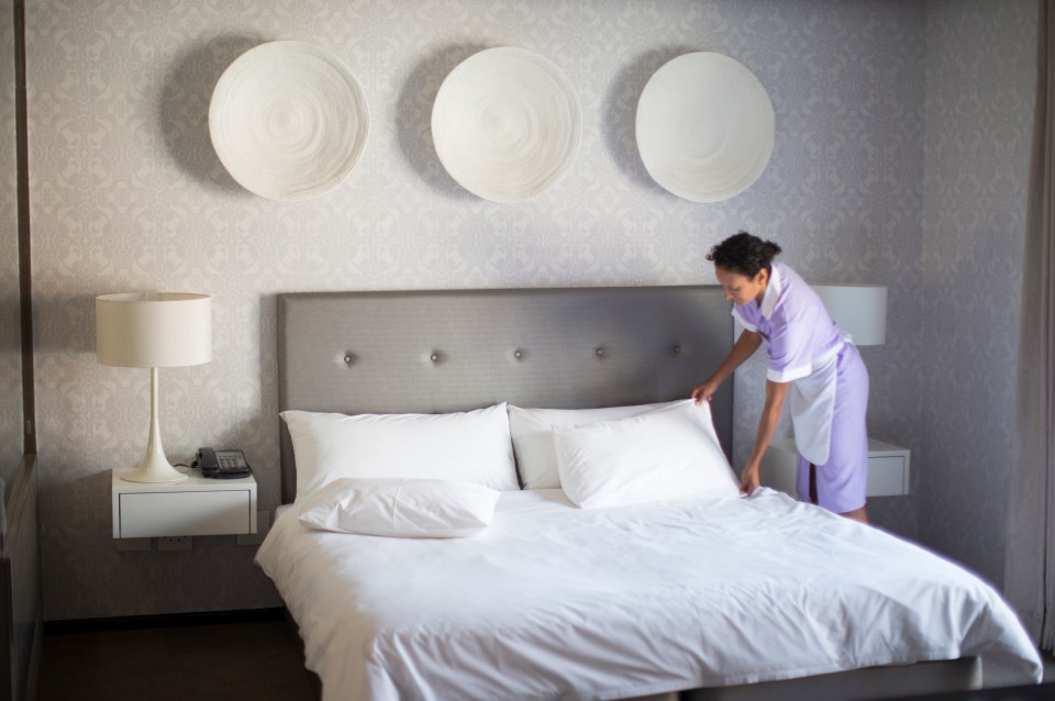 Chambermaid making bed in hotel room