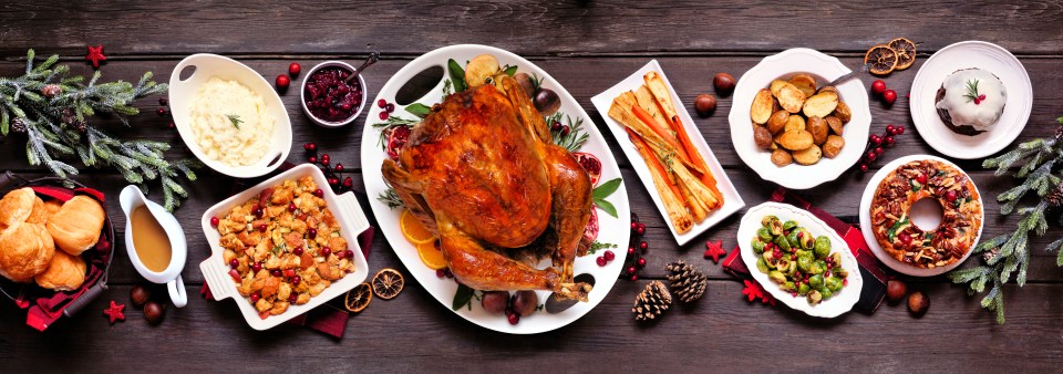 Traditional Christmas turkey dinner. Top view panoramic table scene on a dark wood banner background. Turkey, potatoes and sides, stuffing, fruit cake and plum pudding.; Shutterstock ID 1856131345; purchase_order: -; job: -; client: -; other: -