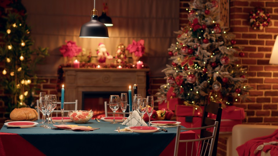 Empty traditional Christmas dinner table inside decorated living room with holiday garlands and dinnerware. Interior of traditional and authentic season cozy setting celebrating religious event.; Shutterstock ID 2196193765; purchase_order: -; job: -; client: -; other: -