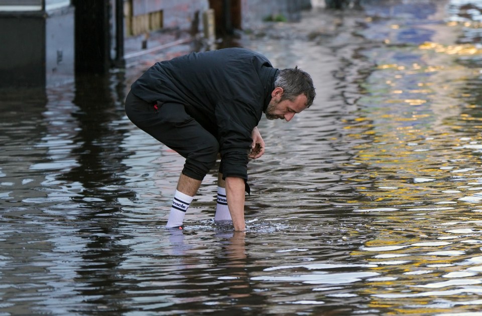 A shopkeeper clears the drain in the street in Worthing this morning