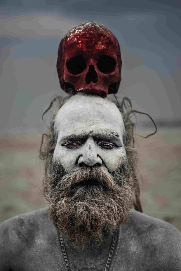 A red-stained skull sits atop the head of an Aghori man