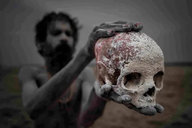 An Aghori man is pictured holding a skull between his hands