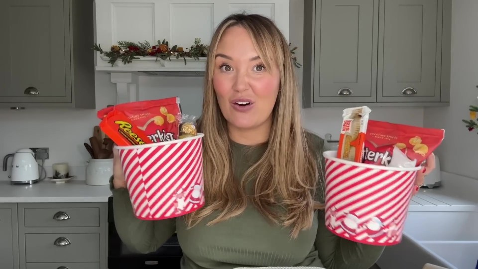 Woman holding two Christmas gift baskets filled with snacks and chocolates.