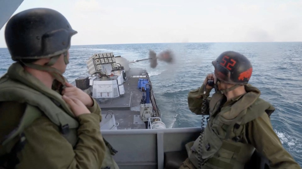 Israeli soldiers watch as their gunboat fires at a target in Gaza