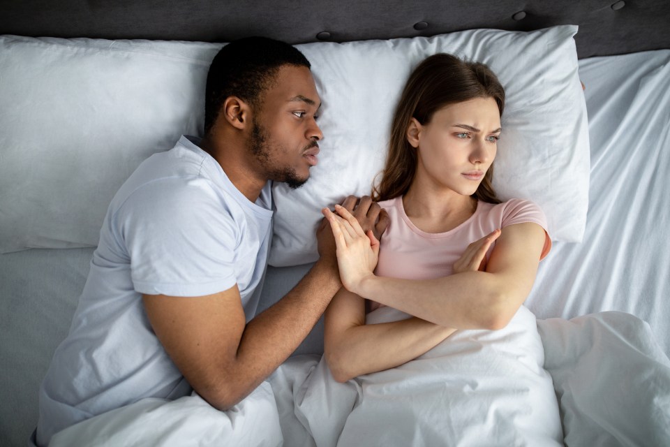 Sexual apathy concept. African American guy touching his upset girlfriend in bed, woman refusing him, top view. Young black couple having difficulties in sex, suffering from relationship problems