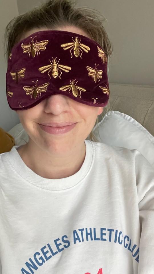 Woman wearing a burgundy sleep mask with gold bees.