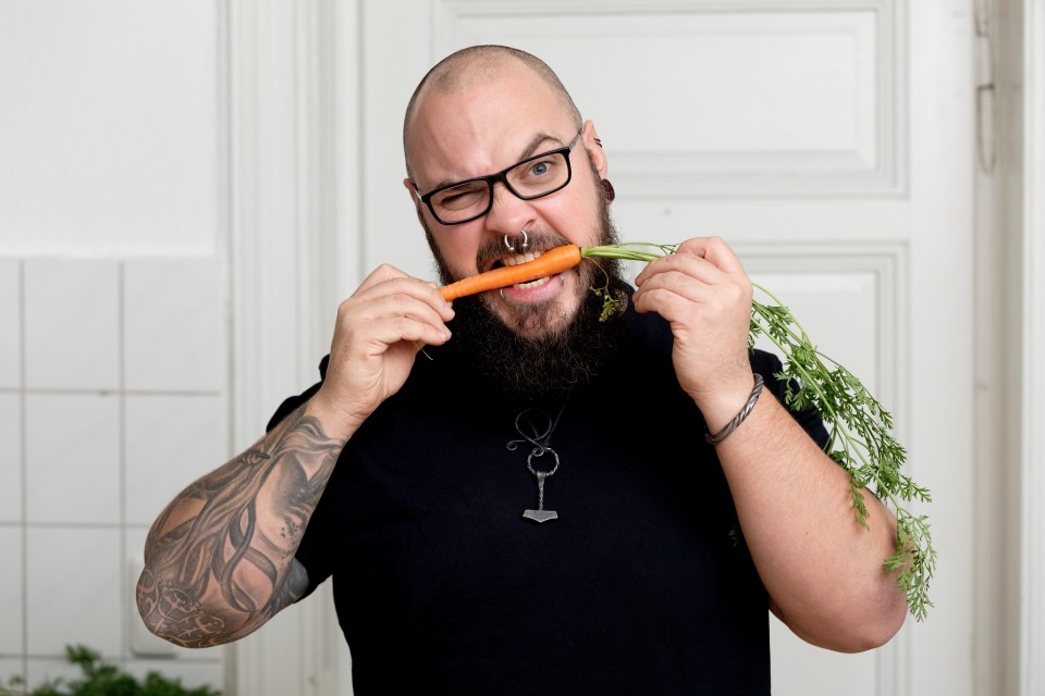 Portrait of bearded man biting in carrot in kitchen