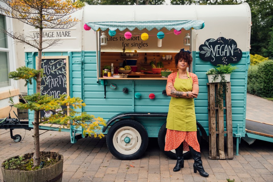 Outside a food truck where a mixed race female hipster stands confidently in front of the truck looking to the camera with her arms folded in front of her.