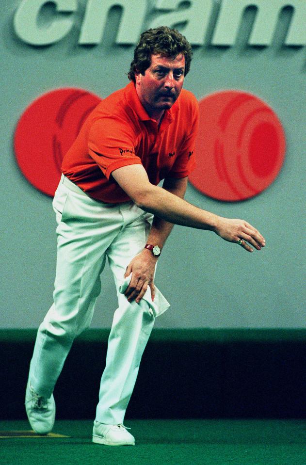 A man in an orange shirt and white pants bowls.