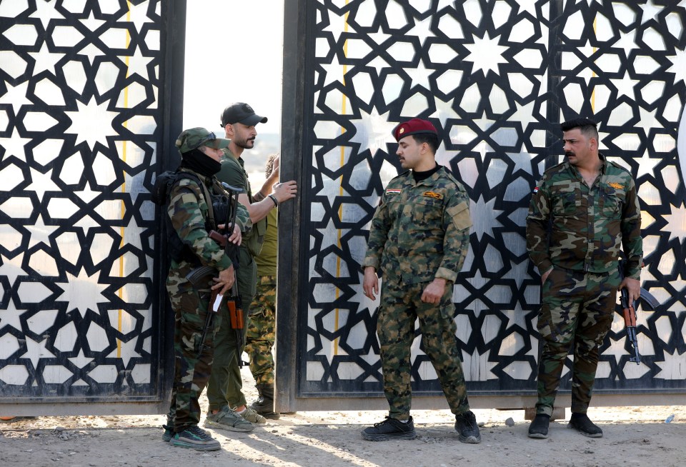 Members of Iraqi Shiite Popular Mobilization Forces (PMF) stand near a gate after a reported drone attack